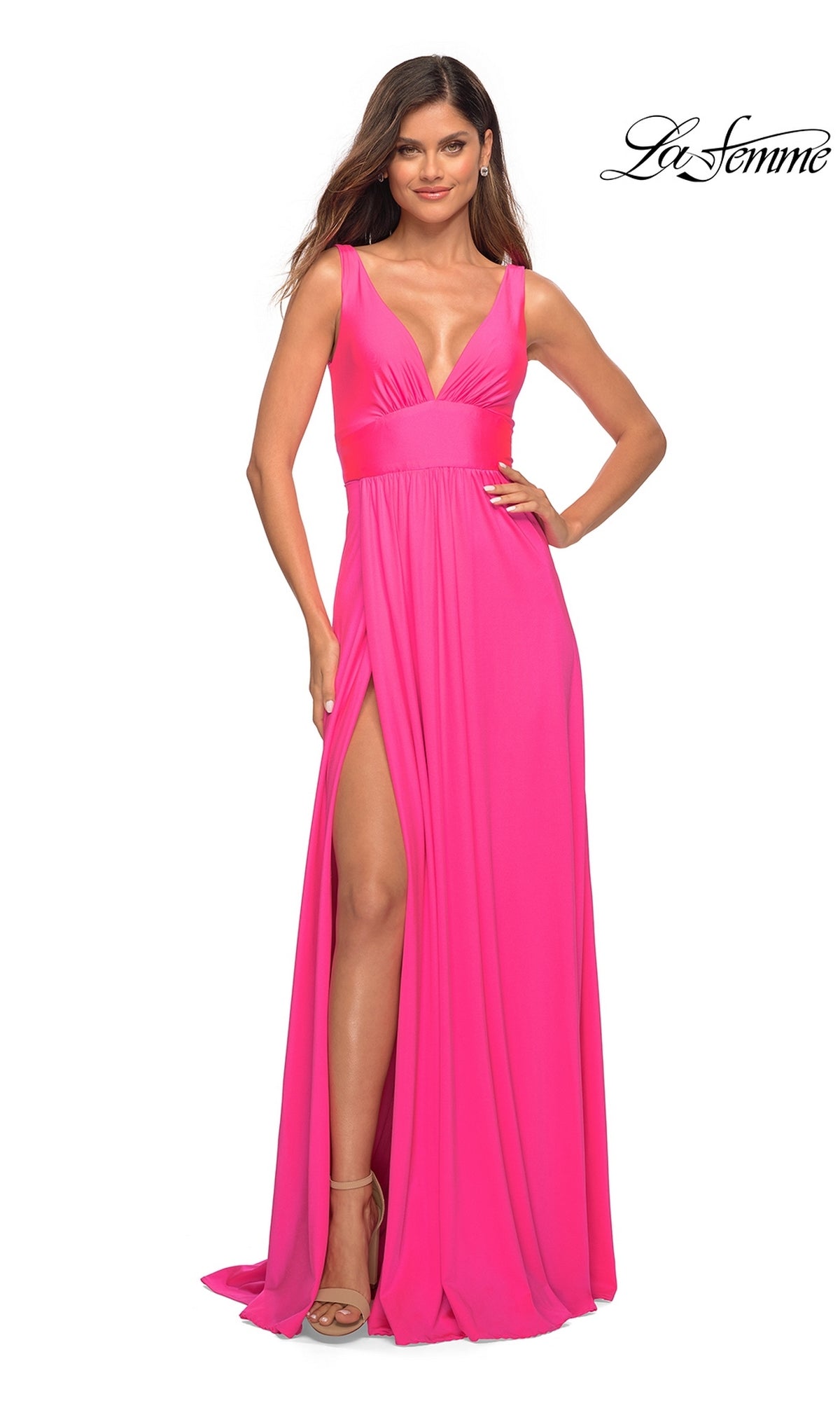 A woman stands confidently with one hand on her hip in the La Femme Neon Pink Long A-Line Prom Dress 30669, featuring a sleeveless design, floor-length skirt, deep V-neckline, and a high slit.